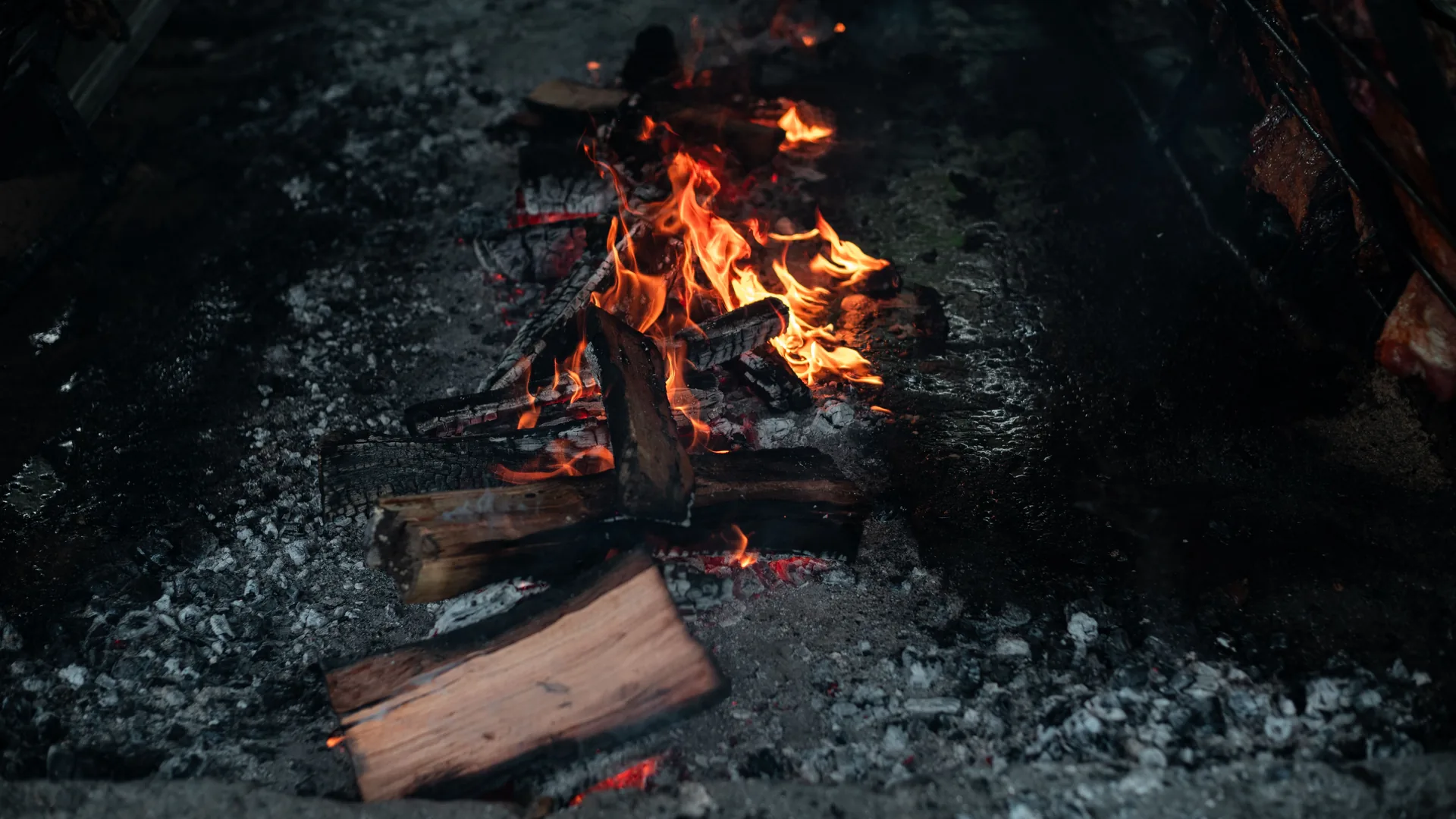 Wood embers and open flame under a traditional Argentine asado grill